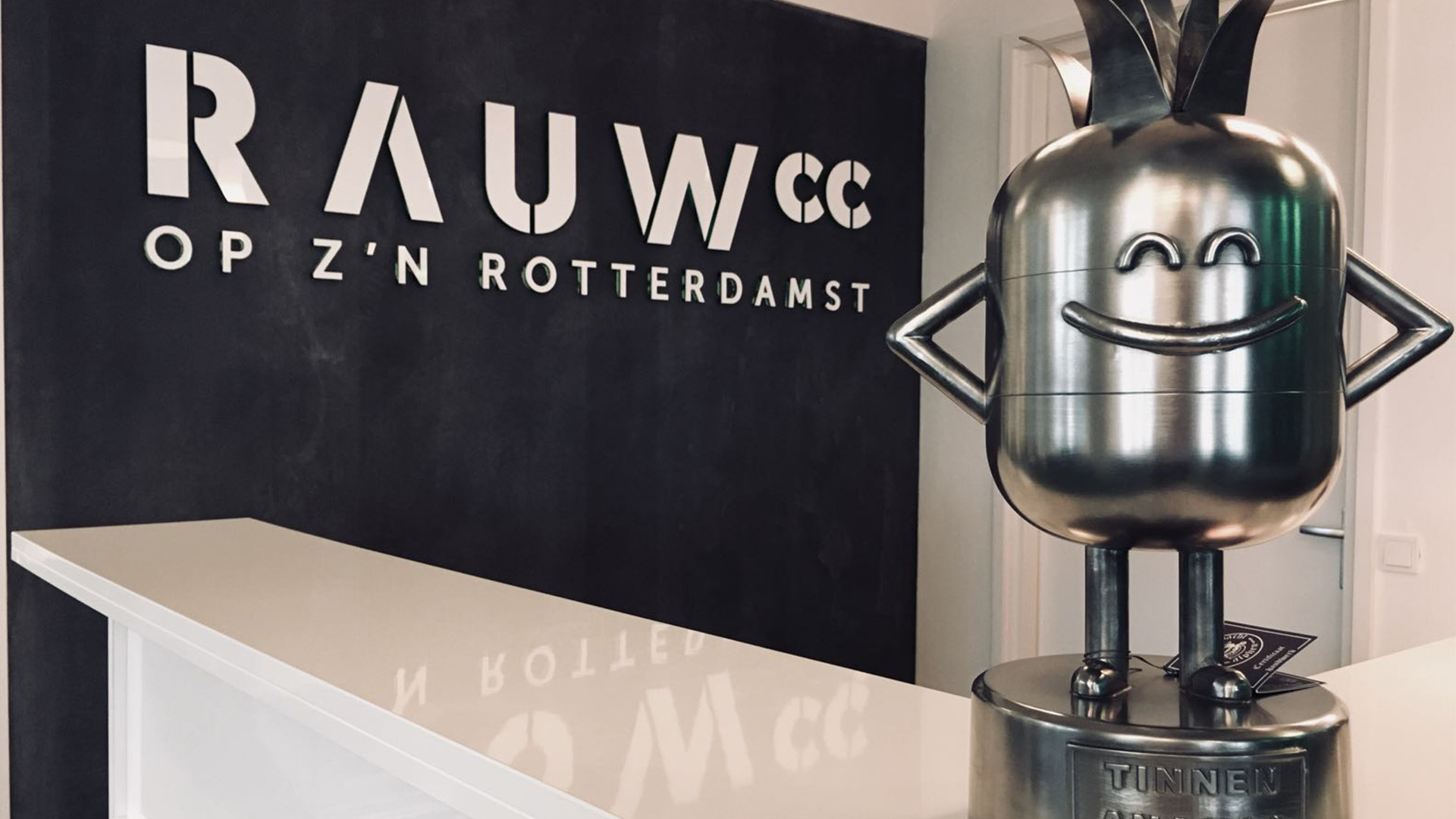 De Tinen Ananas award bij RAUWcc op kantoor, op de achtergrond het RAUWcc logo