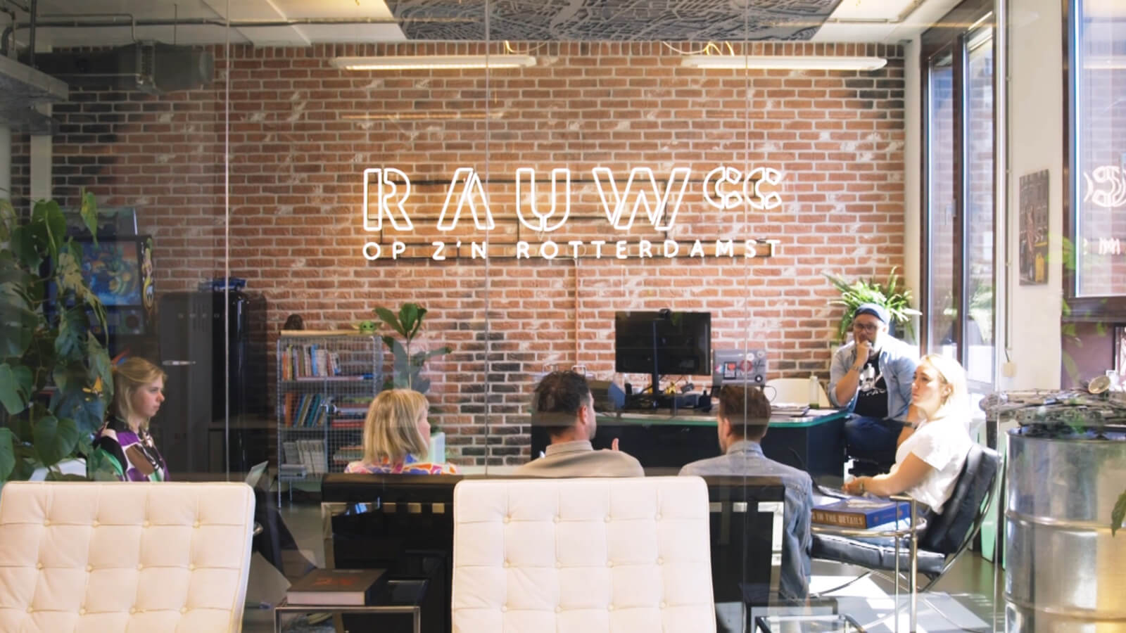 Creatieve RAUWcc meeting op kantoor. Aan een bakstenen muur hangt een RAUWcc logo dat oplicht.