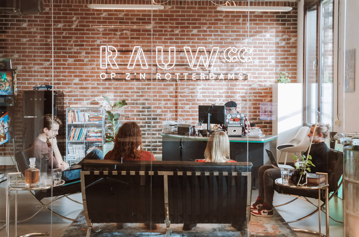 Creatieve RAUWcc meeting op kantoor. Aan een bakstenen muur hangt een RAUWcc logo dat oplicht.